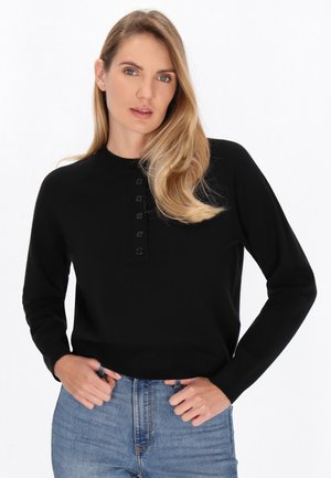 Black sweater with a round neckline, long sleeves, and a button placket featuring five black buttons. Worn with blue high-waisted jeans.