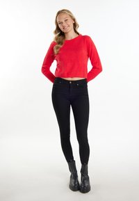 Rode cropped trui gemaakt van een pluizig materiaal, gecombineerd met zwarte high-waisted skinny jeans en zwarte enkellaarsjes. Eenvoudig ontwerp, zonder patronen.