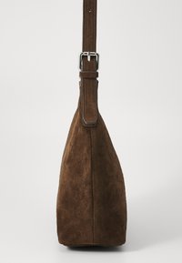 Braune Wildleder-Handtasche von der Seite gezeigt, mit einem verstellbaren Riemen und silberner Schnalle vor einem schlichten Hintergrund.