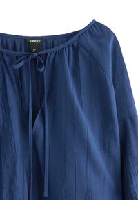 Mörkblå blus med vertikala ränder, rund halsringning och knutet rosett-detalj framtill, märkt storlek small av Lindex.