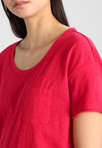 Red, short-sleeve t-shirt with a round neckline and a chest pocket. Soft, lightweight fabric with a smooth texture.