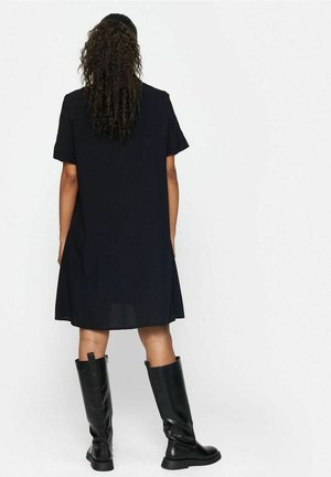 Robe noire à manches courtes avec une coupe ample, dotée d'un ourlet droit et d'un tissu léger. Assortie à des bottes noires à hauteur de genoux.