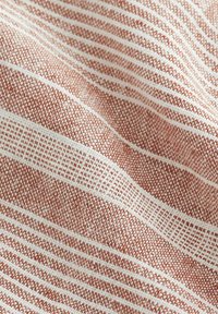 Tissu textile avec une texture douce, présentant des rayures horizontales alternées de couleur rouille et blanche ainsi qu'un motif en grille.