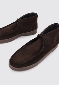 Botines de ante marrón con punta redonda, detalles de cordones y parte superior texturizada. Forro interior suave y suela de goma para mayor comodidad.