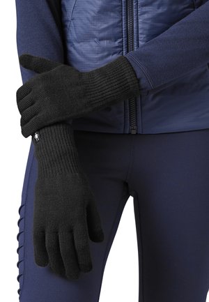 Black knit gloves with ribbed cuffs, worn on hands, paired with a navy blue jacket and pants, showcasing a protective and fitted design.