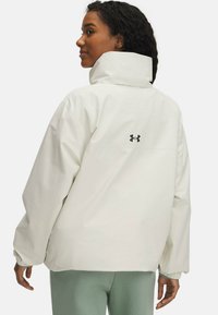 White waterproof jacket with a high collar, elastic cuffs, and a black logo on the back. Smooth texture and relaxed fit.