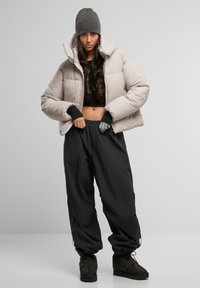 Puffer jacket in light beige with high collar, paired with black baggy pants. Model wears a gray beanie and matching gloves.