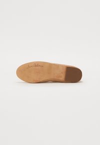 Tan flat shoe sole with a textured edge. Features a smooth, light brown insole with "Sam Edelman" printed, and a subtle pattern on the bottom.