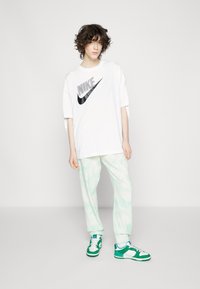 Camiseta blanca de gran tamaño con un logo negro de Nike, pantalones de chándal teñidos de luz en verde claro y zapatillas verdes y blancas con un diseño clásico.