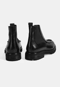 Bottines Chelsea noires avec une tige en cuir lisse, des panneaux élastiques sur les côtés et une semelle en caoutchouc texturée. Présente un tirette à l'arrière.