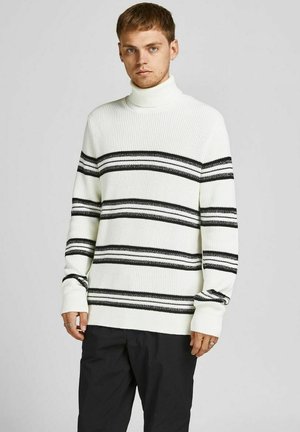 Weißer Strickrollkragenpullover mit schwarzen horizontalen Streifen. Merkmale sind ein strukturiertes Muster und eine lockere Passform, kombiniert mit dunklen Hosen.