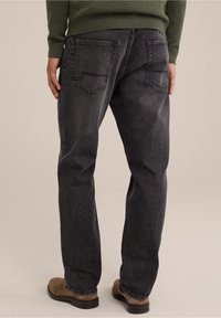 Svarta denimjeans med avslappnad passform och bakfickor, tillsammans med bruna skor. Tyget ser ut att vara texturerat med förstärkt sömnad.