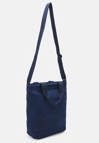 Navy denim tote bag with dual top handles and a detachable shoulder strap. Smooth texture, square shape, and simple design with no visible accents.