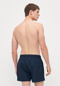 Námornícke plavky s elastickým pásom a bočnými vreckami, vyrobené z ľahkej tkaniny. Strih je nad kolená.