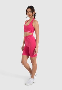 Fuchsia sportbeha en bijpassende shorts met het "SMILODON" logo. Glad, rekbaar materiaal; de beha heeft een ronde hals en de shorts hebben een aansluitend ontwerp.