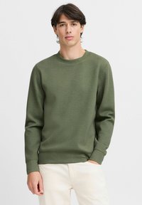 Sudadera verde oliva hecha de una tela suave, con cuello redondo y mangas largas, con puños y dobladillo de canalé. Diseño simple y texturizado.