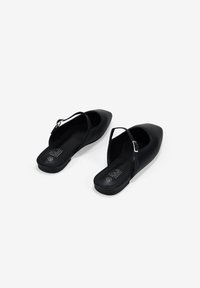 Zapatos planos negros con un diseño de punta afilada, hechos de material sintético suave. Cuentan con una correa ajustable y una plantilla acolchada.