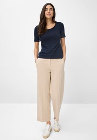 Marineblå kortærmet top kombineret med beigefarvede vidde bukser og hvide sneakers, med en scooped halsudskæring og minimalistisk design.