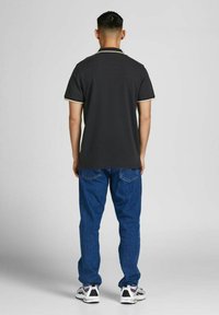 Dark gray short-sleeve polo shirt with contrasting yellow trim at the collar and sleeves, paired with blue jeans and sneakers.