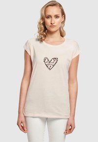 Lys rosa bomulds-t-shirt med optrukne ærmer, med et sort linjet hjerte udfyldt med et leopardmønster i midten.