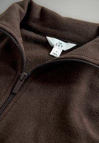 Veste zippée en polaire marron avec col montant, dotée d'une fermeture éclair en métal et d'une étiquette indiquant "THE SET", taille M, fabriquée au Cambodge.