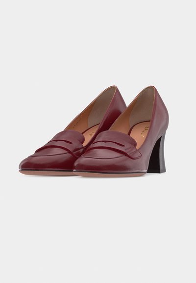 Paire de mocassins en cuir bordeaux à talons hauts, avec un bout pointu et un talon carré, sur fond blanc.