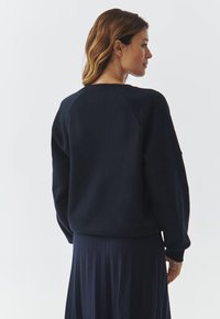 Sweatshirt bleu marine à coupe décontractée, manches raglan et poignets côtelés. Fabriqué en tissu doux avec une texture lisse. Assorti à une jupe plissée.