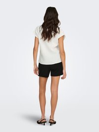 Wit topje met korte mouwen en een gestructureerde stof, gecombineerd met zwarte shorts. Het topje heeft een losse pasvorm en een licht gebogen zoom.