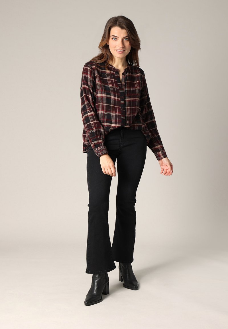 Chemise à carreaux rouge foncé et noir avec une coupe décontractée, associée à un jean évasé noir et des bottines à talons noires.