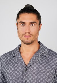 Korte mouwen, overhemd met knopen in donkergrijs, met een geometrisch patroon in lichter grijs. De stof lijkt textuur te hebben met een gladde afwerking.