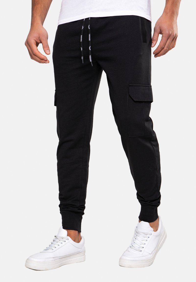 Zwarte cargo joggers met elastische boorden, zijzakken en een trekkoord in de taille. Draagt met witte sneakers. Glad materiaal, casual ontwerp.