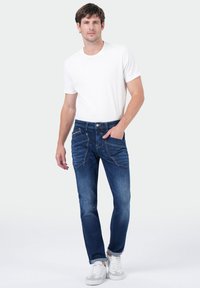 Blauwe denim spijkerbroek met een klassieke snit, voorzien van meerdere zakken en contrasterende stiksels, gecombineerd met een gewoon wit T-shirt en witte sneakers.