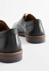 Schwarze Lederschuhe mit glatter Oberfläche, strukturierten Fersenstützen und einer braun-blauen gestuften Sohle. Klassisches, niedriges Design.