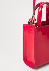 Rode patenten leren handtas met een gestructureerd ontwerp, voorzien van twee korte handvaten en een afneembare schouderband. Accenten in goudkleurig metaal.