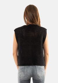 Top negro de punto sin mangas con un diseño suelto y tejido abierto. Presenta un cuello redondo y un corte recto, combinado con jeans gris claro.