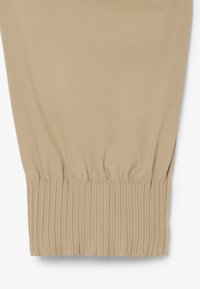 Bein einer beigen Hose mit geripptem elastischem Bündchen, gefertigt aus weichem, gewebtem Stoff mit dezent diagonalem Köpermuster.