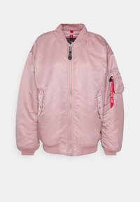 Veste bomber rose clair avec fermeture éclair à l’avant, col côtelé, poignets, deux poches latérales et une poche zippée sur la manche avec une étiquette rouge.