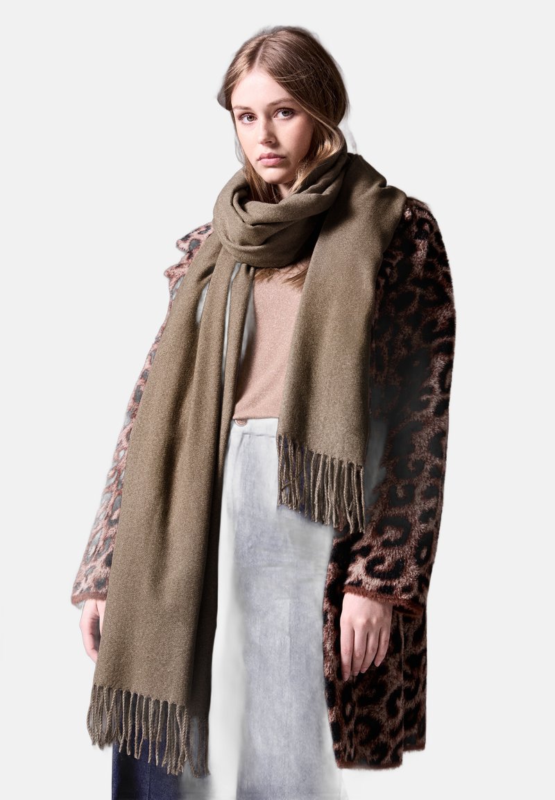 Scarf con frange verde oliva realizzato in materiale morbido, appoggiato su un top marrone chiaro, abbinato a un cappotto con stampa leopardata marrone e nera.