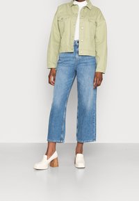 Světlý zelený zkrácený kabát s předními kapsami, kombinovaný s modrými širokými džíny s vysokým pasem. Bílé platformové boty se dřevěnými podpatky.