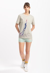 Lichtgrijze katoenen T-shirt met een kleurrijk abstract ontwerp. Korte mouwen, ronde hals, relaxte pasvorm. Draagt met mintgroene shorts en witte sneakers.