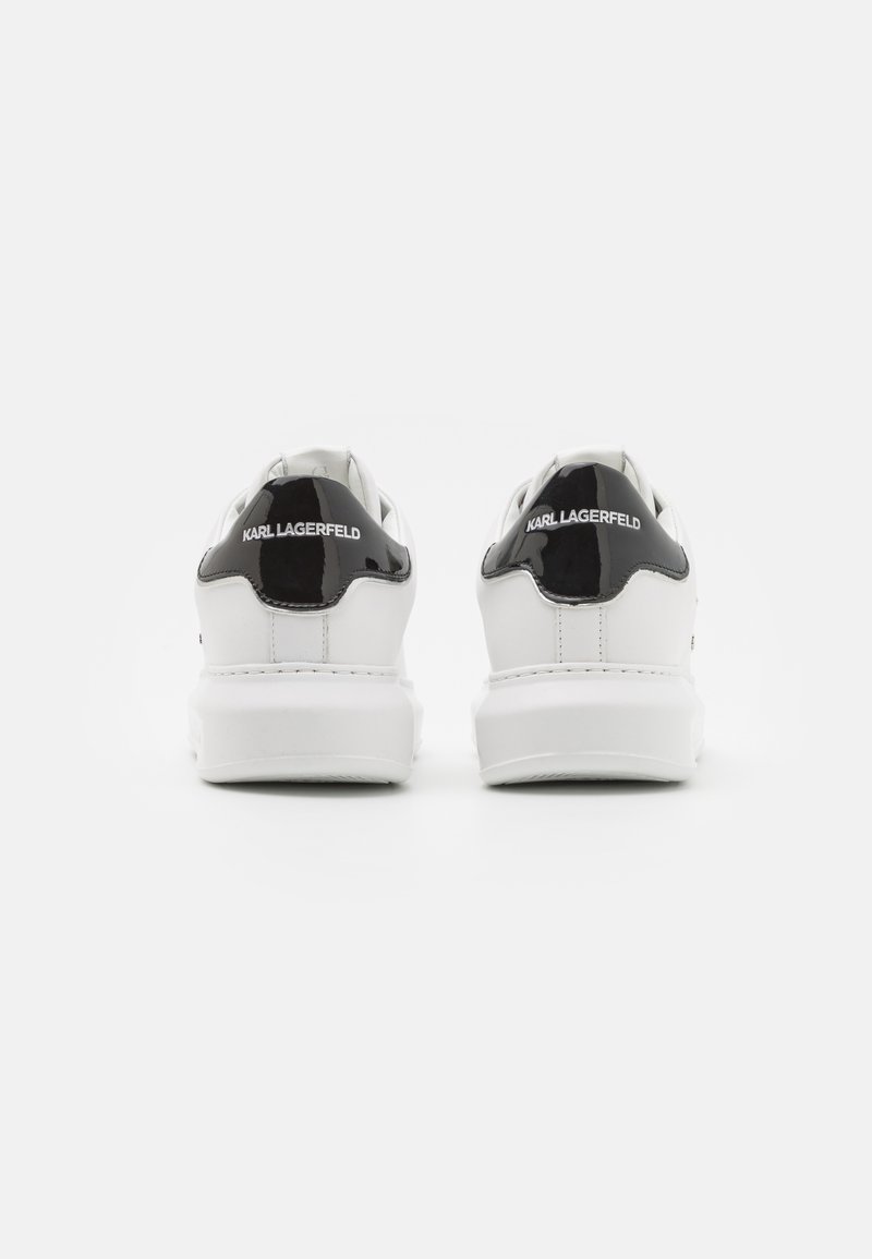 Baskets blanches avec une finition en cuir lisse, accents en cuir verni noir au talon, et logo "Karl Lagerfeld" en blanc à l'arrière.