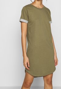 Olive green T-shirt dress with short sleeves, gray rolled cuffs, round neckline, and curved hem. Made of soft, lightweight fabric.