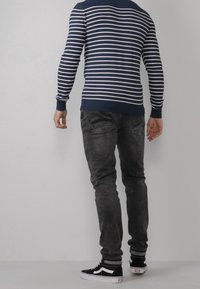 Maglione a righe navy e bianche a maniche lunghe con polsini a coste, abbinato a jeans slim-fit grigio scuro e sneakers nere con dettagli bianchi.