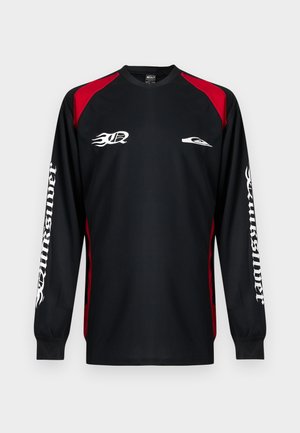 Maillot de sport noir à manches longues avec panneaux rouges aux épaules, logo de flamme blanc sur la poitrine et "Quiksilver" en police gothique blanche sur les deux manches.