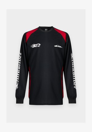 Maillot de sport noir à manches longues avec panneaux rouges aux épaules, logo de flamme blanc sur la poitrine et "Quiksilver" en police gothique blanche sur les deux manches.