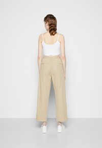 Beige weite-Hosen mit hoher Taille und Gesäßtaschen, kombiniert mit weißen Sneakern. Der Stoff wirkt glatt mit einer strukturierten Passform.