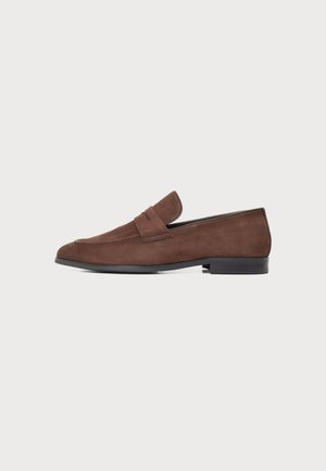 Brun herre loafer i ruskind med flad sort sål og enkel remdetalje, vist fra siden på en neutral baggrund.