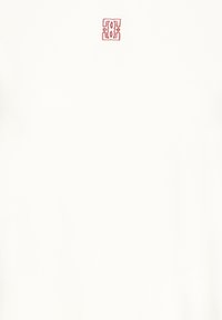 Vêtement blanc avec un petit emblème décoratif rouge centré près de l'encolure sur un fond uni.