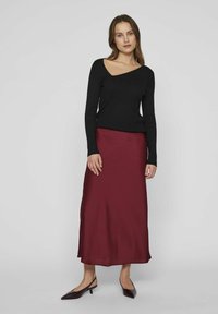 Top noir à manches longues côtelé associé à une jupe midi en satin bourgogne, présentant une texture lisse et un léger brillant. Des ballerines pointues viennent parfaire le look.