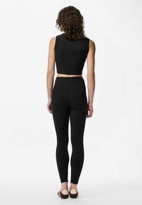 Svart kortärmad topp utan ärmar parsad med högmidjade svarta leggings, båda gjorda av mjuk, töjbar tyg. Har en sömlös design.